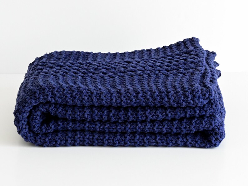 May include: A navy blue knitted throw blanket folded on a white surface.