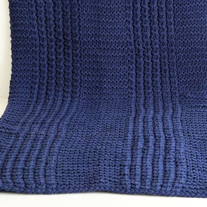 May include: A navy blue knitted throw blanket with a textured cable knit pattern.
