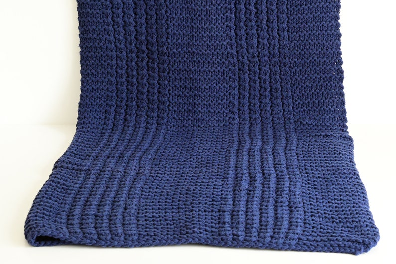 May include: A navy blue knitted throw blanket with a textured cable knit pattern.