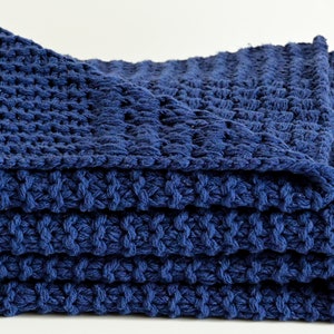 May include: A folded navy blue knitted throw blanket with a textured weave.