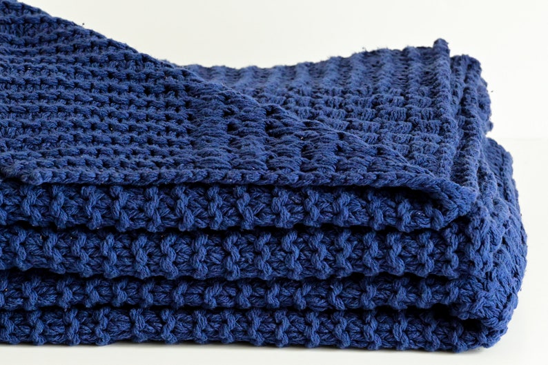 May include: A folded navy blue knitted throw blanket with a textured weave.