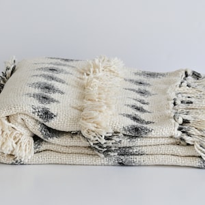 Peut inclure: Une couverture blanche pliée avec un motif géométrique noir et une bordure en franges.