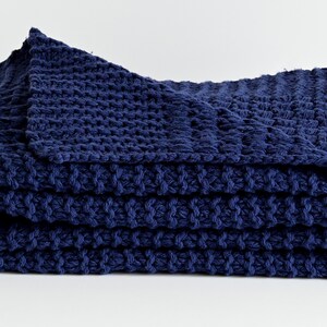 May include: A navy blue knitted throw blanket folded on a white surface. The blanket has a textured, waffle-like pattern.