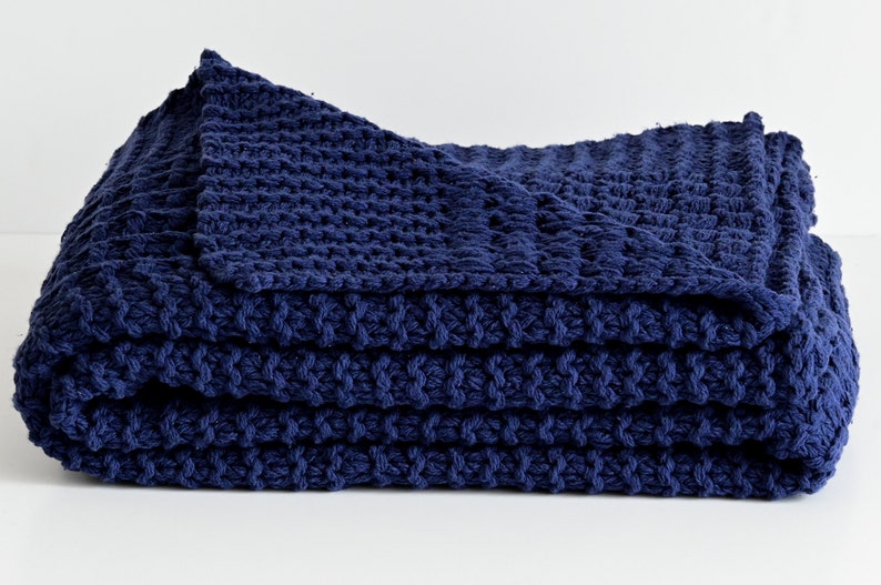 May include: A navy blue knitted throw blanket folded on a white surface. The blanket has a textured, waffle-like pattern.