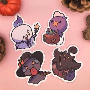 May include: Four Halloween-themed stickers featuring cartoon ghost characters. One holds a star wand, another carries a candy-filled bag. The stickers are in shades of purple, brown, and white, with black outlines. A small pumpkin and pinecones are in the background.