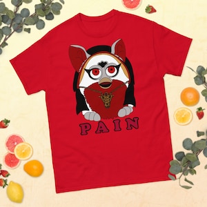 May include: Red t-shirt with a cartoon image of a white furry creature with red eyes wearing a necklace and a crown. The text "PAIN" is printed below the image.