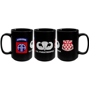 May include: Three black coffee mugs with different military insignia. The first mug has the Airborne symbol with the text "AIRBORNE" and "U.S.". The second mug has the U.S. Paratrooper symbol with the text "U.S. PARATROOPER". The third mug has a shield with the text "I CONTAIN THE MIGHT".