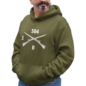 May include: A green hooded sweatshirt with a white graphic of two crossed rifles and the text "3 504 B".