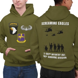 May include: A green hooded sweatshirt with a military theme. The front features a patch with an eagle and the words "Airborne" and "Strike". The back features the words "Screaming Eagles", a silhouette of soldiers, and the text "2-502nd Infantry Rgt. 101st Airborne Division".