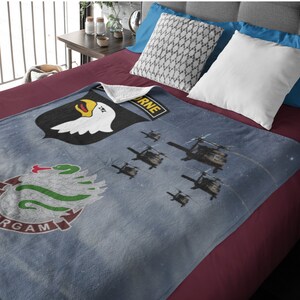 May include: A blue fleece blanket with a white eagle, green snake, and the words "101st Airborne" and "Screaming Eagles". The blanket features a starry night sky background with silhouettes of helicopters.