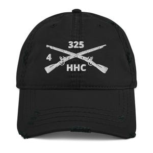 May include: Black distressed baseball cap with white embroidered crossed rifles and the text "325", "4", and "HHC". The cap has a curved brim and a worn, vintage look.