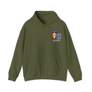 May include: A green hooded sweatshirt with a pocket on the front. The sweatshirt has an embroidered patch with two shields and the text "AIRBORNE" and "LET'S GO".