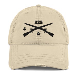 May include: A beige distressed baseball cap with a black embroidered design of two crossed rifles, the number "325", and the letter "A".