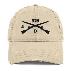 May include: A beige distressed baseball cap with a black embroidered design of two crossed rifles with the text "325 4 D".