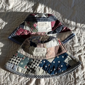 May include: Two patchwork bucket hats with a blue and white checkered trim. Both hats have a label that reads "Northern Homemakers".