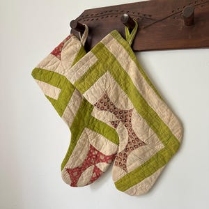 Könnte beinhalten: Zwei gesteppte Weihnachtsstrümpfe mit einem Patchwork-Design in den Farben Limettengrün, Creme und gemustertem Rot. Die Strümpfe sind aus genähten geometrischen Paneelen gefertigt und verfügen über eine Stoffschlaufe zum Aufhängen.