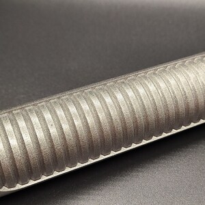 May include: Close-up of a silver metal rod with a textured, ribbed surface. The rod is smooth and shiny.
