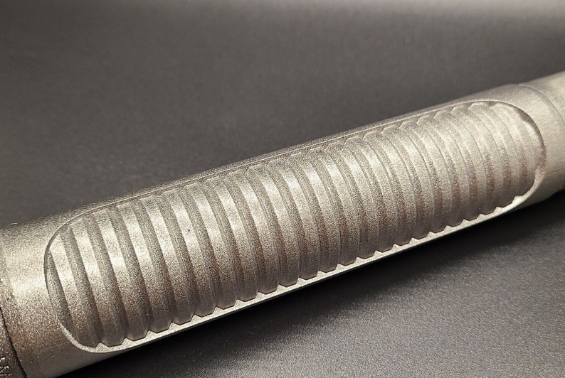 May include: Close-up of a silver metal rod with a textured, ribbed surface. The rod is smooth and shiny.