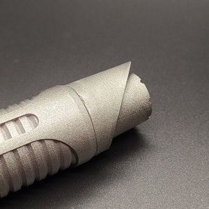 May include: A silver lightsaber hilt with a textured surface and a ribbed design. The hilt has a curved end and a black accent.
