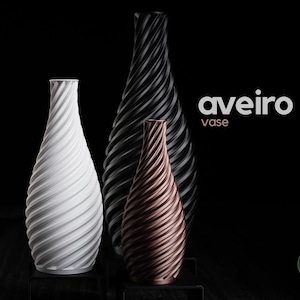Pode incluir: Três vasos com design em espiral em tons de branco, preto e bronze, contra um fundo preto. Os vasos têm uma superfície texturizada e canelada e uma forma esguia e alongada. As palavras "aveiro" e "vase" são exibidas em texto branco.