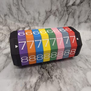 May include: A colorful, segmented puzzle toy with numbers 6, 7, and 8 printed on each segment. The segments are arranged in a rainbow color pattern, with black end pieces. The numbers are white.