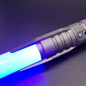 May include: A black lightsaber with a blue blade and a red button. The lightsaber has a charging port and a textured grip.