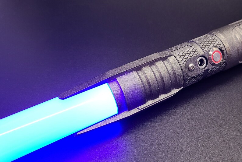 May include: A black lightsaber with a blue blade and a red button. The lightsaber has a charging port and a textured grip.