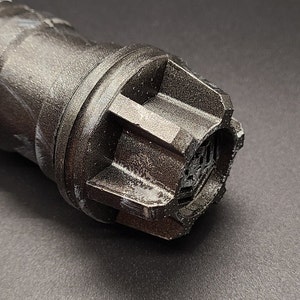 Pu&ograve; includere: Primo piano di un'impugnatura di spada laser nera con una superficie testurizzata e marmorea. L'impugnatura ha un tappo esagonale con un piccolo design intricato.