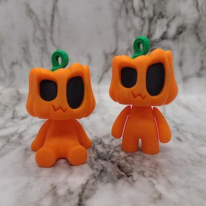 May include: Two orange pumpkin-shaped figurines with black eyes and a green stem. The figurine on the left is sitting down, while the figurine on the right is standing up.