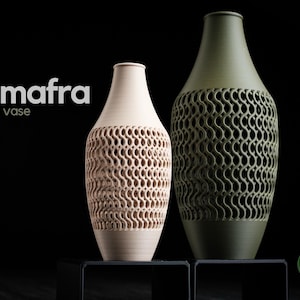 Könnte beinhalten: Zwei dekorative Vasen. Die linke Vase ist beige und die rechte Vase ist olivgrün. Beide Vasen haben ein einzigartiges Lochmuster in der Mitte. Das Wort "mafra" und das Wort "Vase" sind auf der linken Seite des Bildes aufgedruckt.