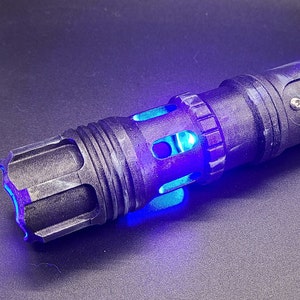 Pu&ograve; includere: Una spada laser nera con una lama di spada laser blu. La spada laser ha una finitura nera testurizzata e un jack audio argentato e un pulsante sul lato.