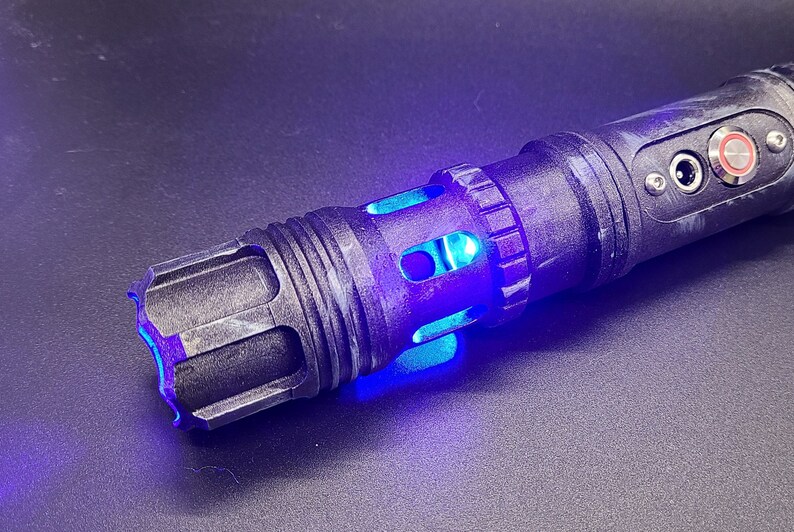 Pu&ograve; includere: Una spada laser nera con una lama di spada laser blu. La spada laser ha una finitura nera testurizzata e un jack audio argentato e un pulsante sul lato.