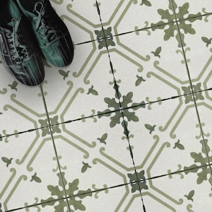 May include: A pair of black and green athletic shoes resting on a floor covered in square tiles. The tiles feature a white base with a repeating olive green floral and geometric pattern that creates a continuous design across the surface.