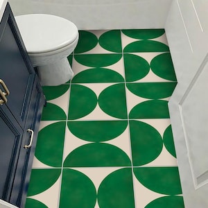 Könnte beinhalten: Grün-cremefarbene Fliesen mit Muster in einem Badezimmer. Die Fliesen zeigen ein sich wiederholendes Design aus grünen Halbkreisen auf cremefarbenem Hintergrund. Eine weiße Toilette und ein dunkelblauer Schrank sind sichtbar.