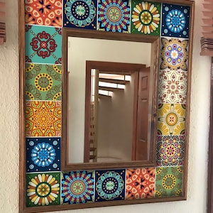 May include: A square wall mirror featuring a wooden frame decorated with a border of colorful, patterned square tiles. The tiles display various intricate geometric and floral designs in shades of blue, orange, yellow, green, and white.