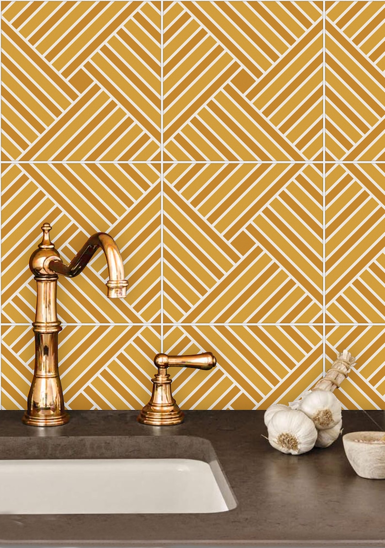 May include: A kitchen sink with a gold faucet and a tiled backsplash featuring a geometric pattern of white lines on a mustard yellow background. There are three heads of garlic on the counter next to a small wooden bowl.