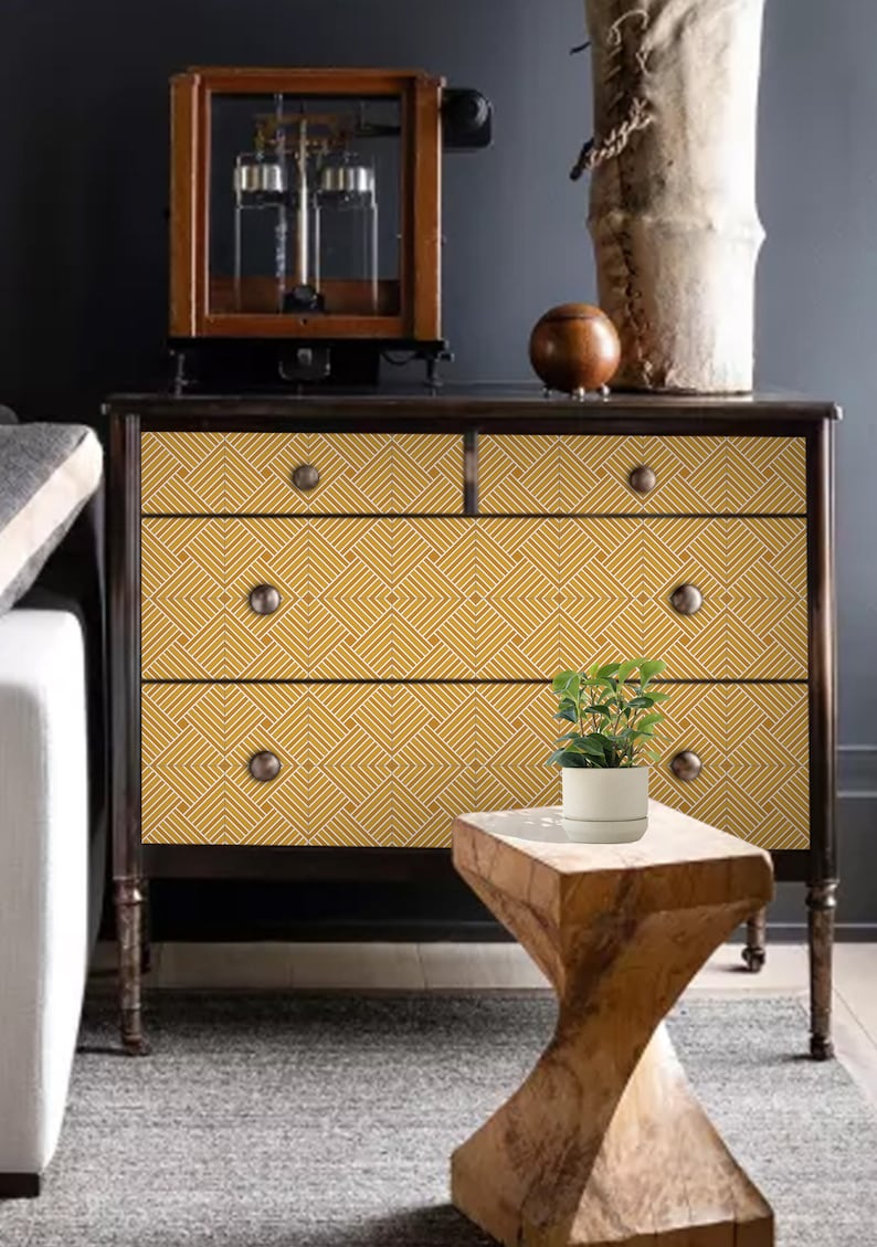 May include: A dark wood dresser with three drawers. The drawers are covered with a yellow and white geometric pattern. A small potted plant sits on a wooden stool in front of the dresser.