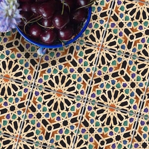 May include: A close-up of a patterned tile floor with a bowl of cherries on top. The tiles are black, brown, green, and blue with a geometric pattern. The bowl is blue and white.