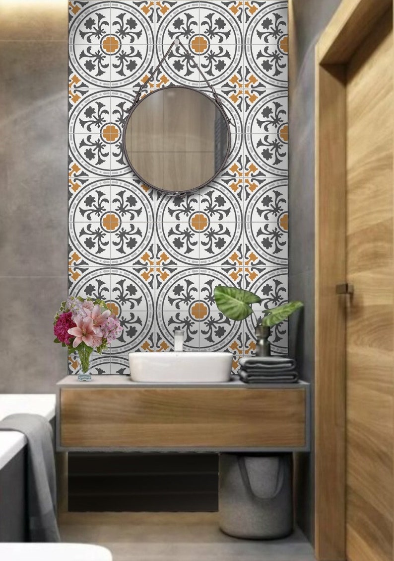 May include: A white bathroom vanity with a gray countertop and a round mirror. The vanity has a wooden cabinet with a gray sink and a gray wastebasket. The wall behind the vanity is tiled with white and black patterned tiles with orange accents.