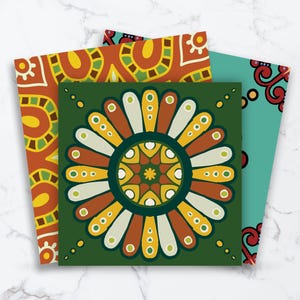 May include: Three square art prints featuring intricate patterns. The front print displays a dark green background with a large, symmetrical, multi-colored floral mandala design in shades of yellow, orange, white, and light green.