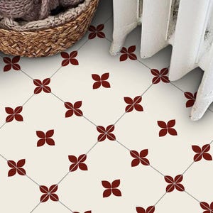 Puede incluir: Baldosas de suelo color crema con un patrón repetido de formas de flores de cuatro pétalos de color rojo oscuro. Las flores están dispuestas en un patrón de cuadrícula, conectadas por finas líneas grises. Una cesta tejida y una cortina blanca son visibles en el fondo.