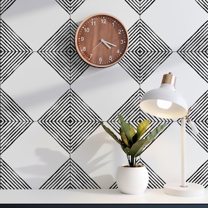 May include: A round wall clock with a wood-grain face and white numbers, a white desk lamp with a gold-toned neck, and a small green potted plant. The background features a white wall with a repeating black geometric diamond line pattern.