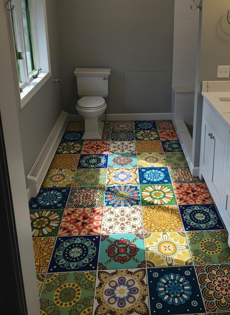 May include: A bathroom floor covered in square tiles featuring a variety of colorful, intricate mandala-style patterns in shades of blue, yellow, green, orange, and red. The floor is situated in a room with gray walls, a white toilet, and a white vanity.