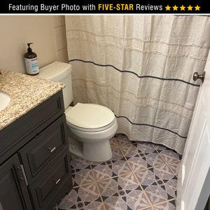 May include: A bathroom with a white toilet, a dark gray vanity with drawers, and a white shower curtain with black stripes. The floor is tiled with a geometric pattern in shades of pink, black, and white.