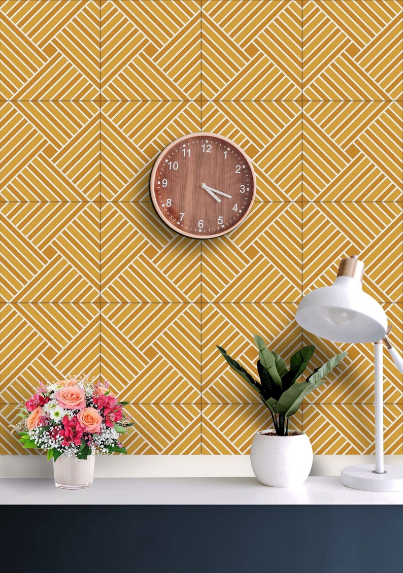 May include: A yellow and white geometric patterned wall with a wooden clock, a potted plant, and a lamp on a shelf. The clock has a wooden frame and black hands. The plant is in a white pot. The lamp is white with a white shade.