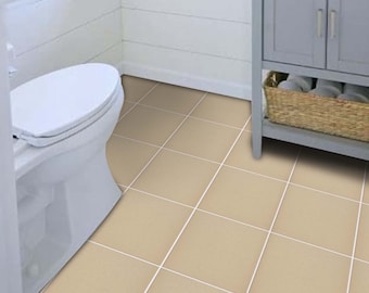 Puede incluir: Un baño con suelo de baldosas cuadradas beige y lechada blanca. La habitación cuenta con un inodoro blanco, un mueble gris con una cesta de mimbre y una pared con paneles blancos. También se ven una ventana y una toalla.