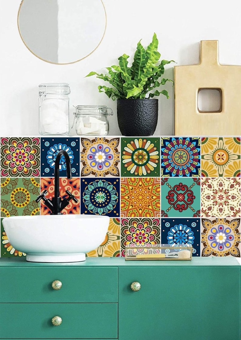 Puede incluir: Un conjunto de azulejos cuadrados para pared con una variedad de coloridos patrones de mandala en tonos azul, amarillo, rojo y verde. Los azulejos est&aacute;n dispuestos en una cuadr&iacute;cula detr&aacute;s de un lavabo de cer&aacute;mica blanca con grifo negro y mueble verde.