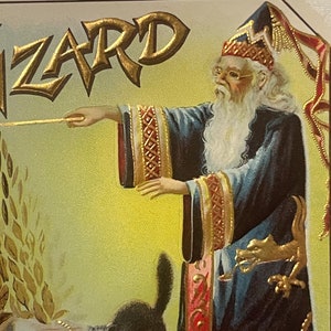 May include: A vintage illustration of a wizard with a long white beard, wearing a blue robe with gold trim and a pointed hat. He is holding a wand in his right hand and pointing it towards a black cat with green eyes. The background is a yellow-gold color with the word "WIZARD" in gold lettering.