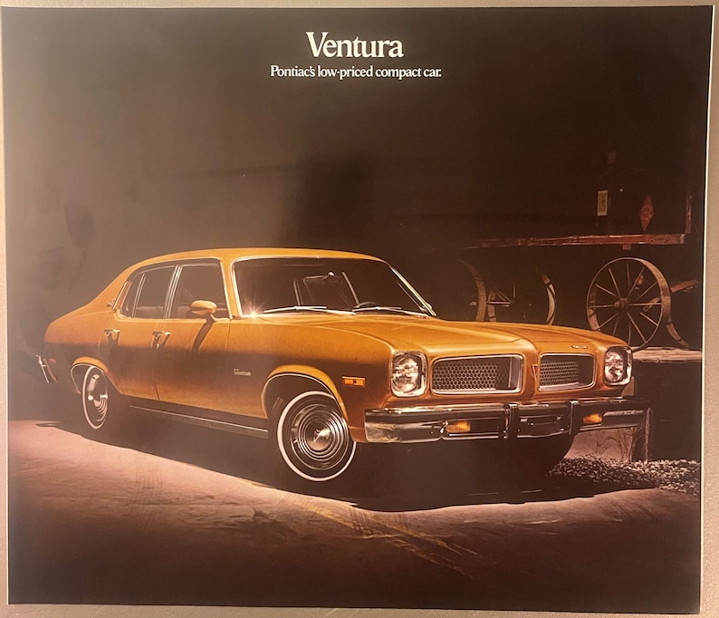 May include: An advert for the Pontiac Ventura, a low-priced compact car. The car is a golden-yellow colour with chrome accents and white-walled tyres. The background is dark, with the car illuminated by a spotlight. The text "Ventura" is at the top.