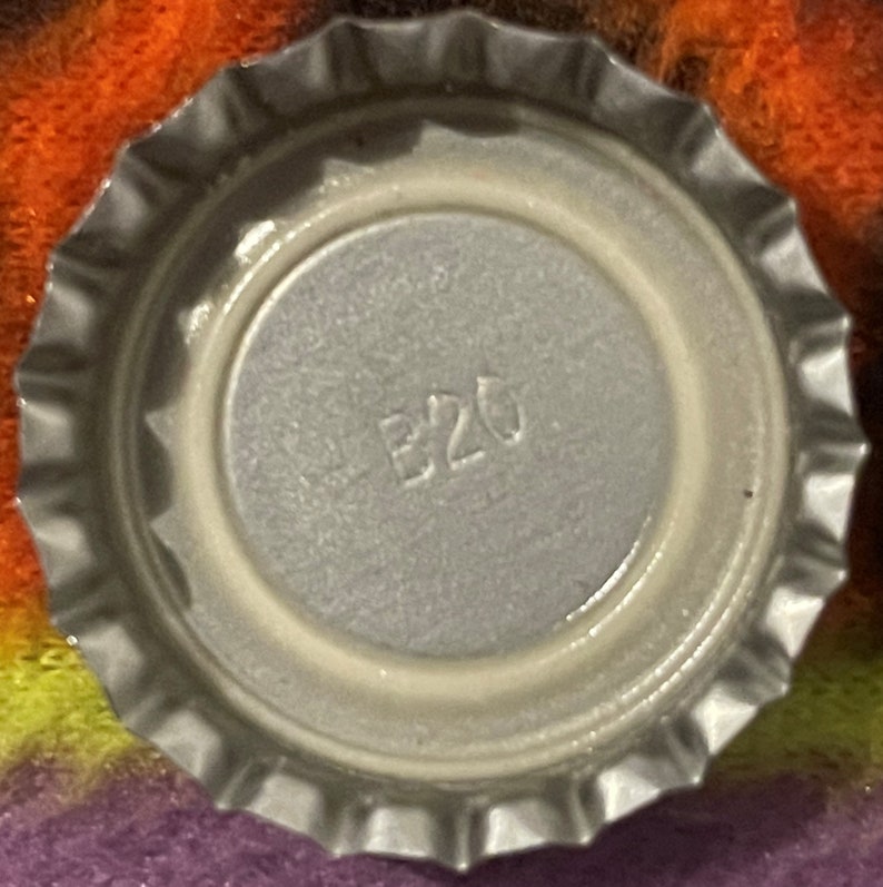 Op de afbeelding: Close-up van een zilveren dop met het nummer "B20" erop gedrukt.